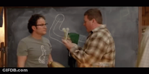 Two Men Are Standing In Front Of A Chalkboard With A Drawing Of A Penis On It GIF