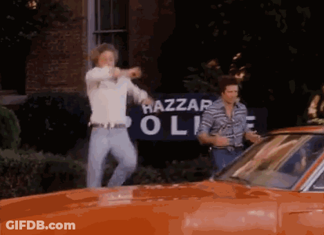 Two Men Are Standing In Front Of A Hazzard Police Sign GIF