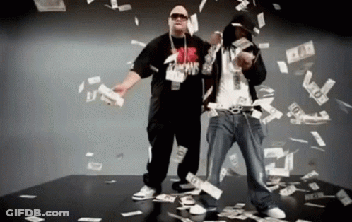 Two Men Are Standing In Front Of A Pile Of Money And One Of Them Is Wearing A Shirt That Says ' Famous ' On It GIF
