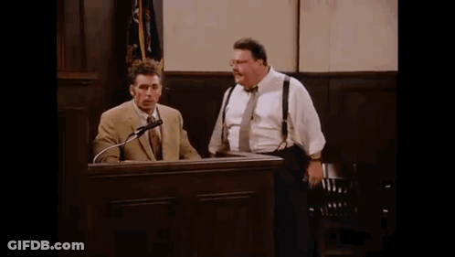 Two Men Are Standing In Front Of A Podium In A Courtroom Talking Into Microphones . GIF