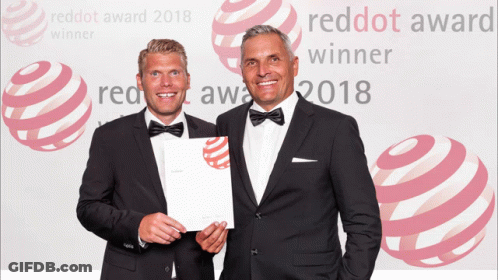 Two Men Are Standing In Front Of A Red Dot Award 2018 Background GIF