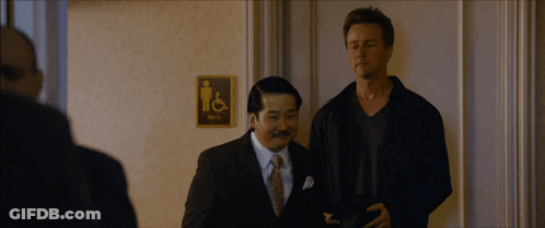 Two Men Standing In Front Of Men's Bathroom Sign GIF
