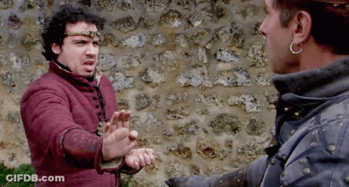 Two Men Are Standing In Front Of A Stone Wall And One Is Wearing A Crown GIF