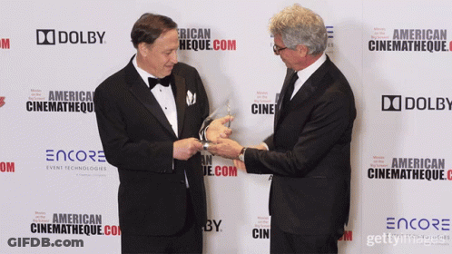 Two Men Are Standing In Front Of A Wall That Says Dolby On It GIF