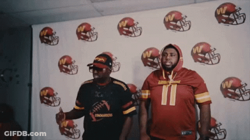 Two Men Are Standing In Front Of A Wall With Football Helmets And One Has The Number 11 On His Jersey GIF