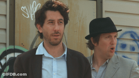 Two Men Are Standing In Front Of A Wall With Graffiti On It That Says Swag GIF