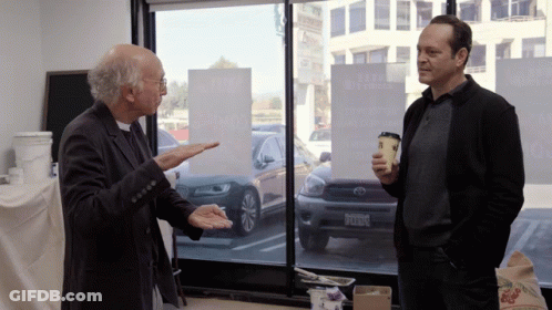 Two Men Are Standing In Front Of A Window With A Sign That Says ' A Few Dollars More ' On It GIF