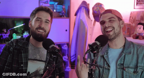 Two Men Are Standing In Front Of Microphones One Is Wearing A Plaid Shirt And The Other Is Wearing A Denim Jacket GIF