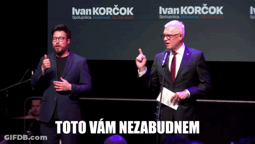 Two Men Are Standing In Front Of Microphones With Ivan Korcok Written On The Screen Behind Them GIF