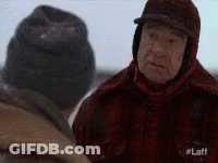 Two Men Are Standing In The Snow And Talking To Each Other . One Of The Men Is Wearing A Hat . GIF