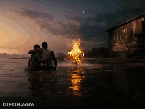 Two Men Are Standing In The Water Looking At A Fire Coming Out Of The Water GIF