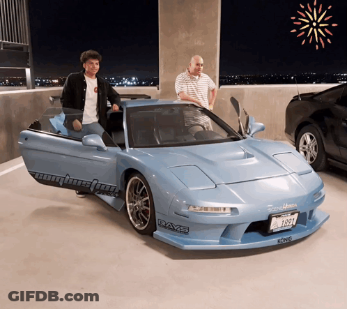 Two Men Are Standing Next To A Blue Sports Car That Says Rays On The Side GIF