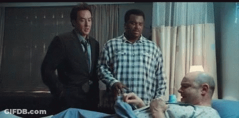 Two Men Are Standing Next To A Man In A Hospital Bed GIF