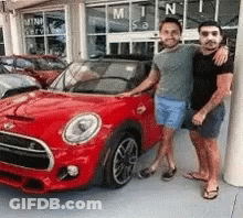 Two Men Are Standing Next To A Red Car In Front Of A Car Dealership . GIF