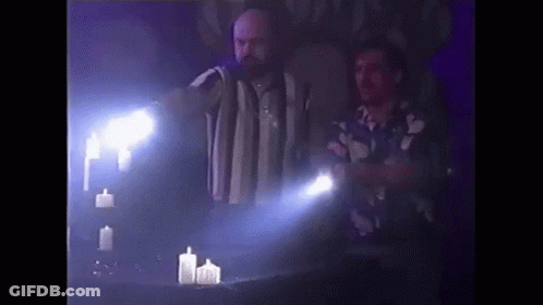 Two Men Are Standing Next To A Table With Candles And A Flashlight . GIF