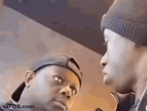 Two Men Are Standing Next To Each Other And Looking At Each Other . One Of The Men Is Wearing A Beanie . GIF