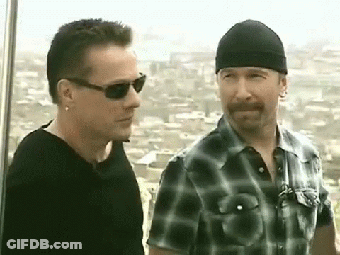 Two Men Are Standing Next To Each Other And Talking . One Of The Men Is Wearing Sunglasses And A Beanie . GIF