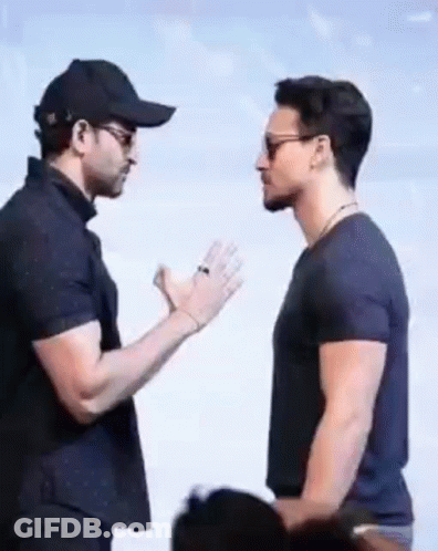 Two Men Are Standing Next To Each Other And Talking To Each Other . One Of The Men Is Wearing A Baseball Cap . GIF