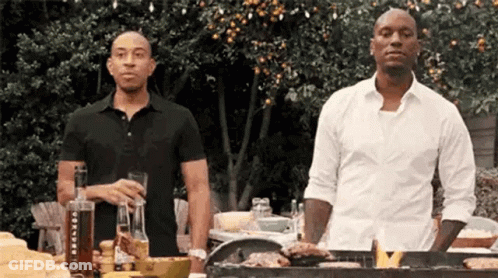 Two Men Are Standing Next To Each Other At A Grill . GIF