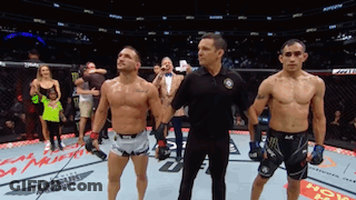 Two Men Are Standing Next To Each Other In A Boxing Ring With A Referee GIF