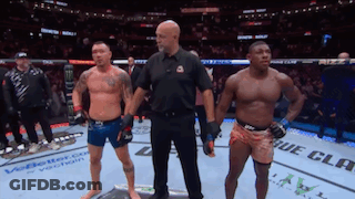 Two Men Are Standing Next To Each Other In A Boxing Ring With A Referee Standing Between Them GIF