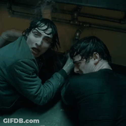 Two Men Are Standing Next To Each Other In A Dark Room And One Is Holding The Other 'S Hand GIF