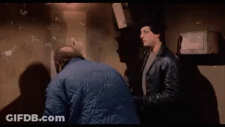 Two Men Are Standing Next To Each Other In A Dark Room And One Of Them Is Holding A Bottle Of Beer . GIF