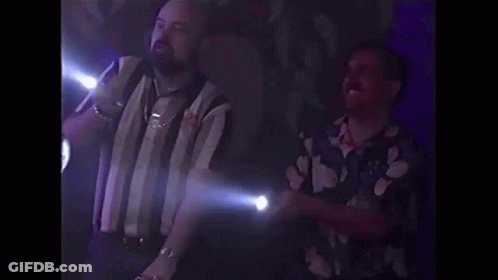 Two Men Are Standing Next To Each Other In A Dark Room . One Of The Men Is Holding A Flashlight . GIF