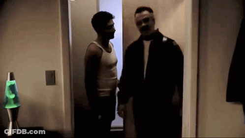 Two Men Are Standing Next To Each Other In A Dark Room With A Green Lava Lamp In The Background . GIF