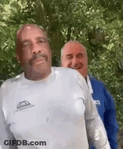 Two Men Are Standing Next To Each Other In A Forest . GIF