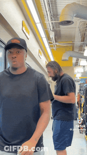 Two Men Are Standing Next To Each Other In A Hallway And One Of Them Has Tiktok Written On His Phone GIF
