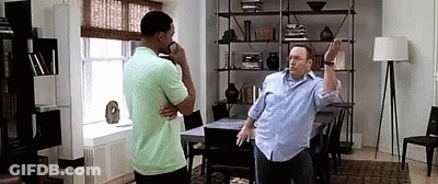 Two Men Are Standing Next To Each Other In A Living Room . One Of The Men Is Talking On A Cell Phone . GIF