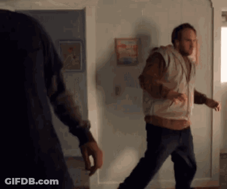 Two Men Are Standing Next To Each Other In A Living Room . One Of The Men Is Wearing A Hoodie . GIF