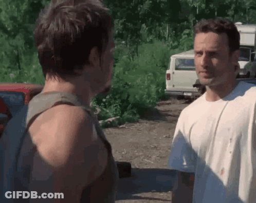 Two Men Are Standing Next To Each Other In A Parking Lot And Talking . GIF