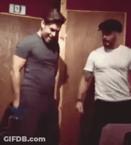 Two Men Are Standing Next To Each Other In A Room . One Of The Men Is Wearing A Hat . GIF
