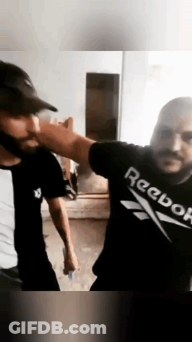 Two Men Are Standing Next To Each Other In A Room Wearing Reebok Shirts . GIF