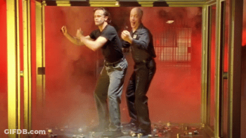 Two Men Are Standing Next To Each Other In A Room With Red Smoke Coming Out Of It . GIF