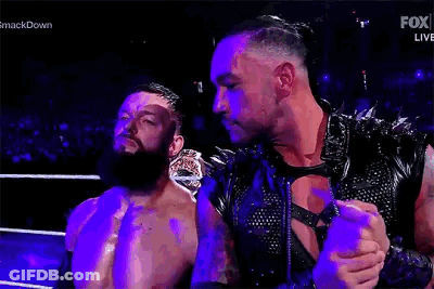 Two Men Are Standing Next To Each Other In A Wrestling Ring . One Of The Men Is Wearing A Leather Vest . GIF