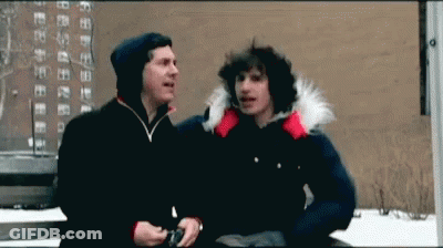 Two Men Are Standing Next To Each Other In Front Of A Building And Talking GIF