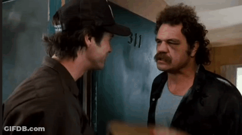 Two Men Are Standing Next To Each Other In Front Of A Door . One Of The Men Is Wearing A Hat . GIF