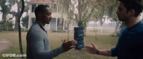 Two Men Are Standing Next To Each Other In Front Of A House . One Of The Men Is Holding A Stack Of Boxes . GIF