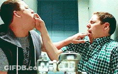 Two Men Are Standing Next To Each Other In Front Of A Mirror And One Of Them Is Licking The Other 'S Face . GIF