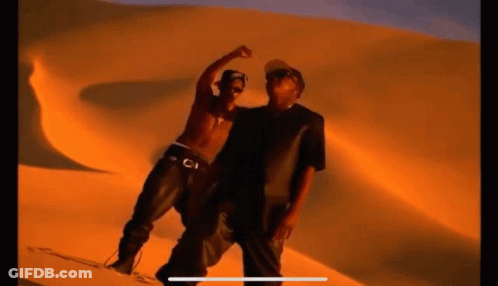 Two Men Are Standing Next To Each Other In Front Of A Sand Dune In The Desert . GIF