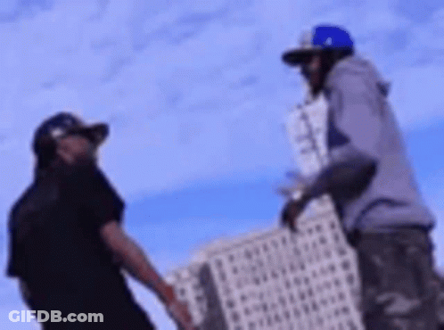 Two Men Are Standing Next To Each Other In Front Of A Tall Building . GIF