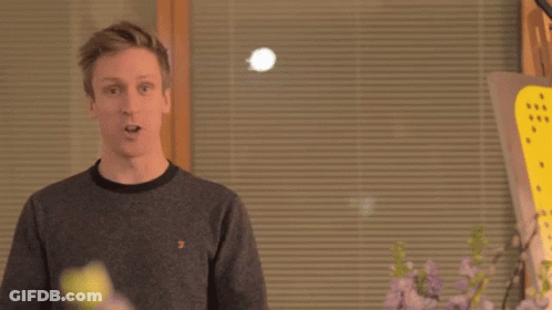 Two Men Are Standing Next To Each Other In Front Of A Window With Blinds And Flowers . GIF