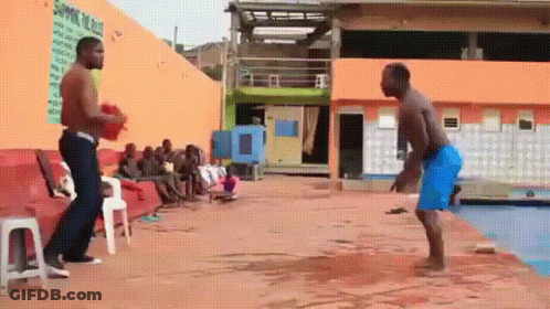 Two Men Are Standing Next To Each Other On A Concrete Surface In Front Of A Pool . GIF