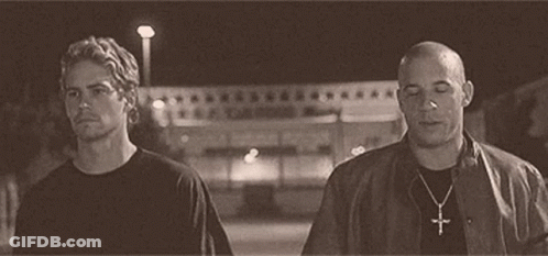 Two Men Are Standing Next To Each Other On A Street At Night . One Of The Men Is Wearing A Cross Necklace . GIF