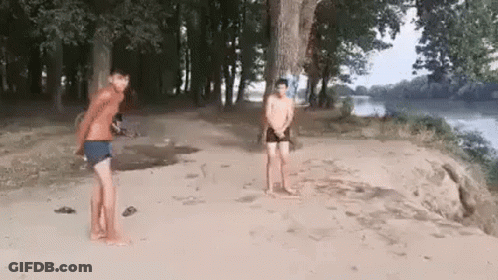 Two Men Are Standing On A Sandy Beach Next To A River . GIF