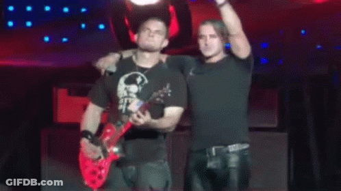 Two Men Are Standing On A Stage With One Holding A Red Guitar GIF