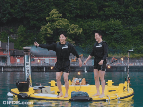 Two Men Are Standing On A Yellow Boat With The Number 80015 On It GIF